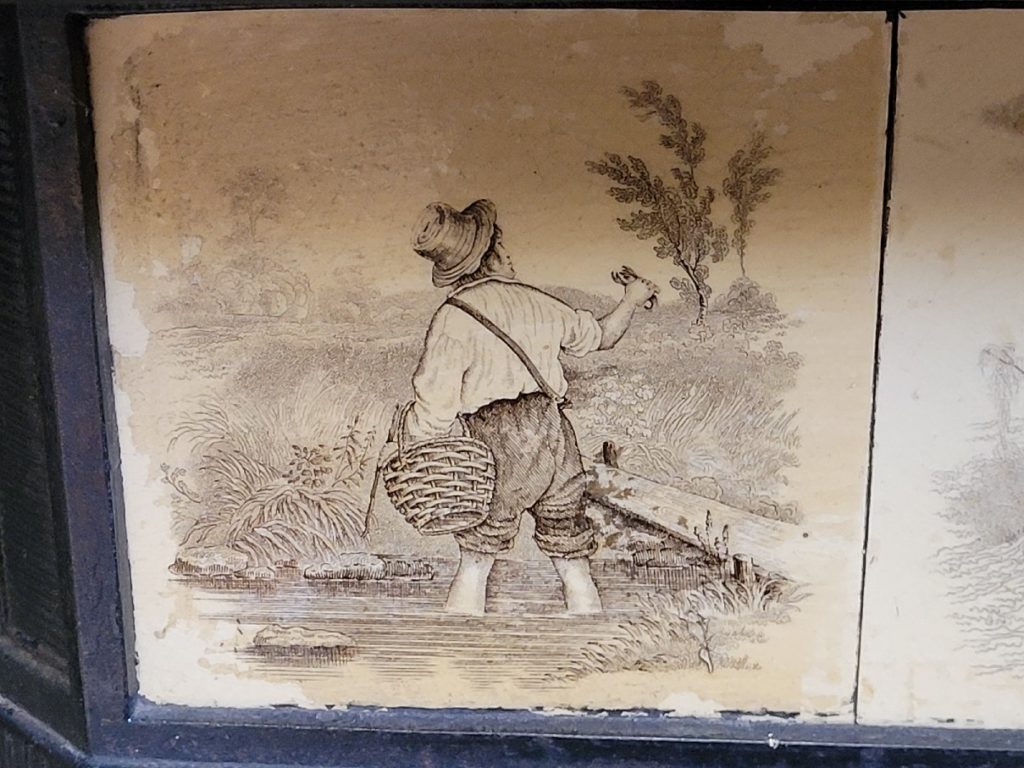 ceramic fireplace decorative insert with painted image of a man wading in a stream with a basket