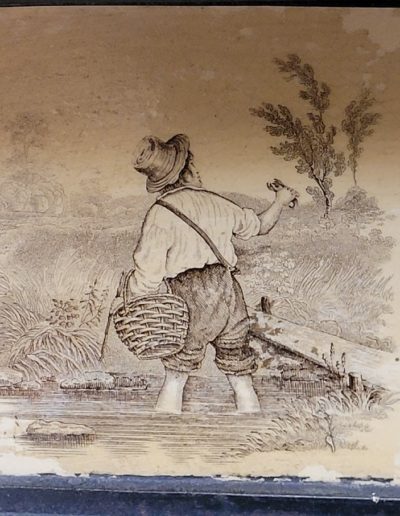 ceramic fireplace decorative insert with painted image of a man wading in a stream with a basket