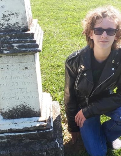 Young man crouching beside his ancestor's gravestone