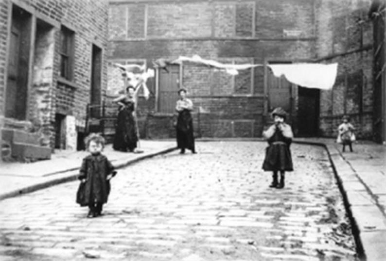 19th century black and white of poor children playing in town streets with laundry hanging on lines between the buildings in the background